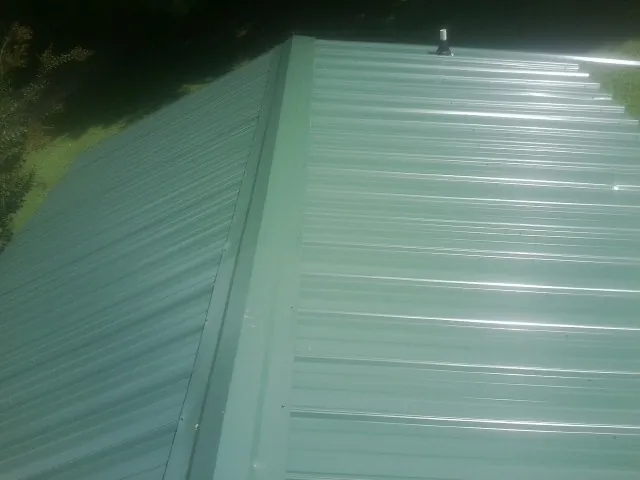 New green metal panels meeting at the ridge of a roof — Flat Roof Repair work by our crew in Pompano Beach